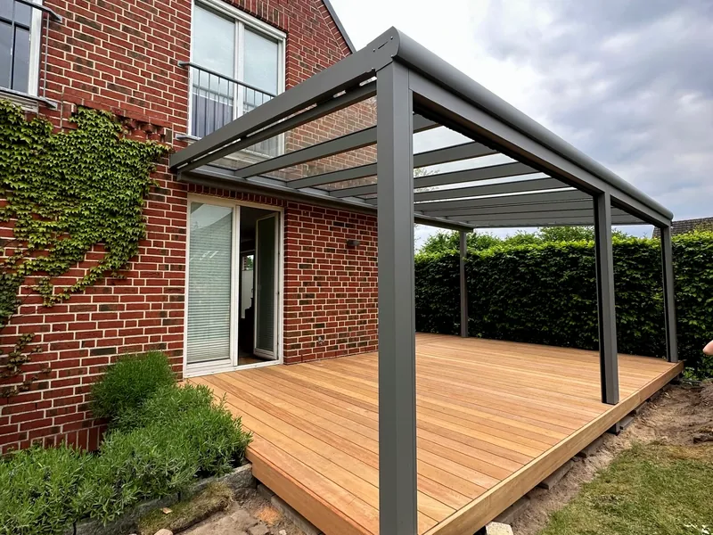 Holzterrasse mit Aluminium-Glas-Überdachung an einer efeubewachsenen Backsteinfassade