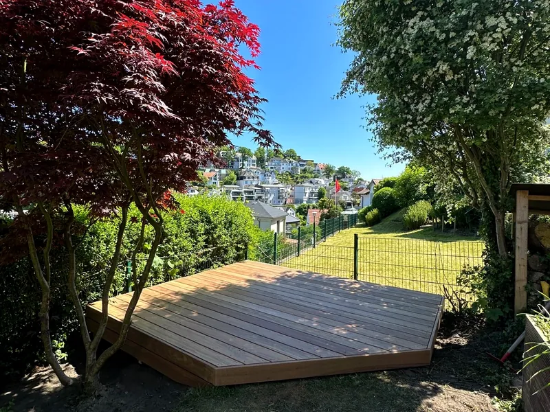 Freistehendes Holzdeck im Garten mit rotem Fächerahorn und Blick über den Hang