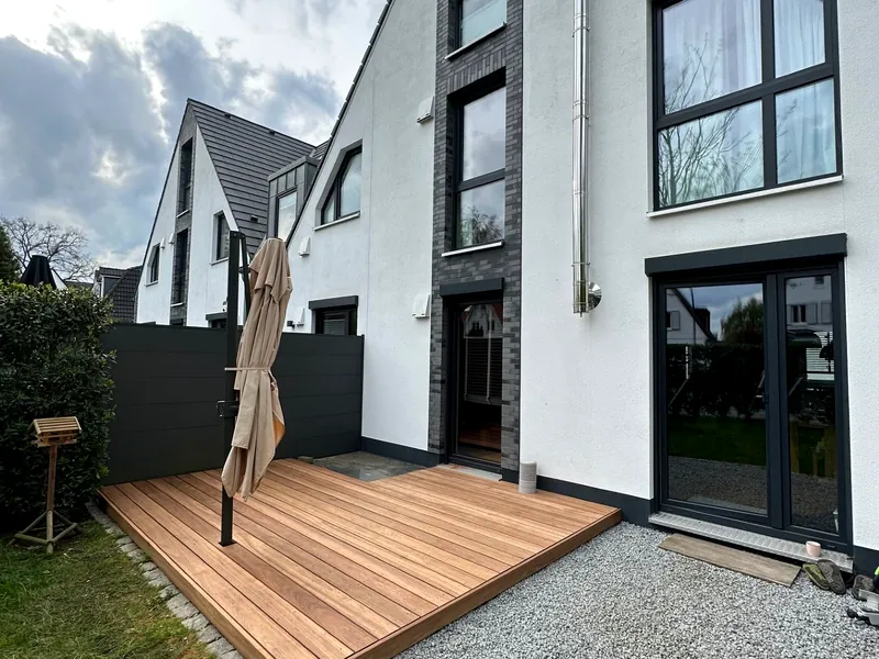 Holzdeck mit Kiesbett an einem weiß verputzten Stadthaus-Neubau